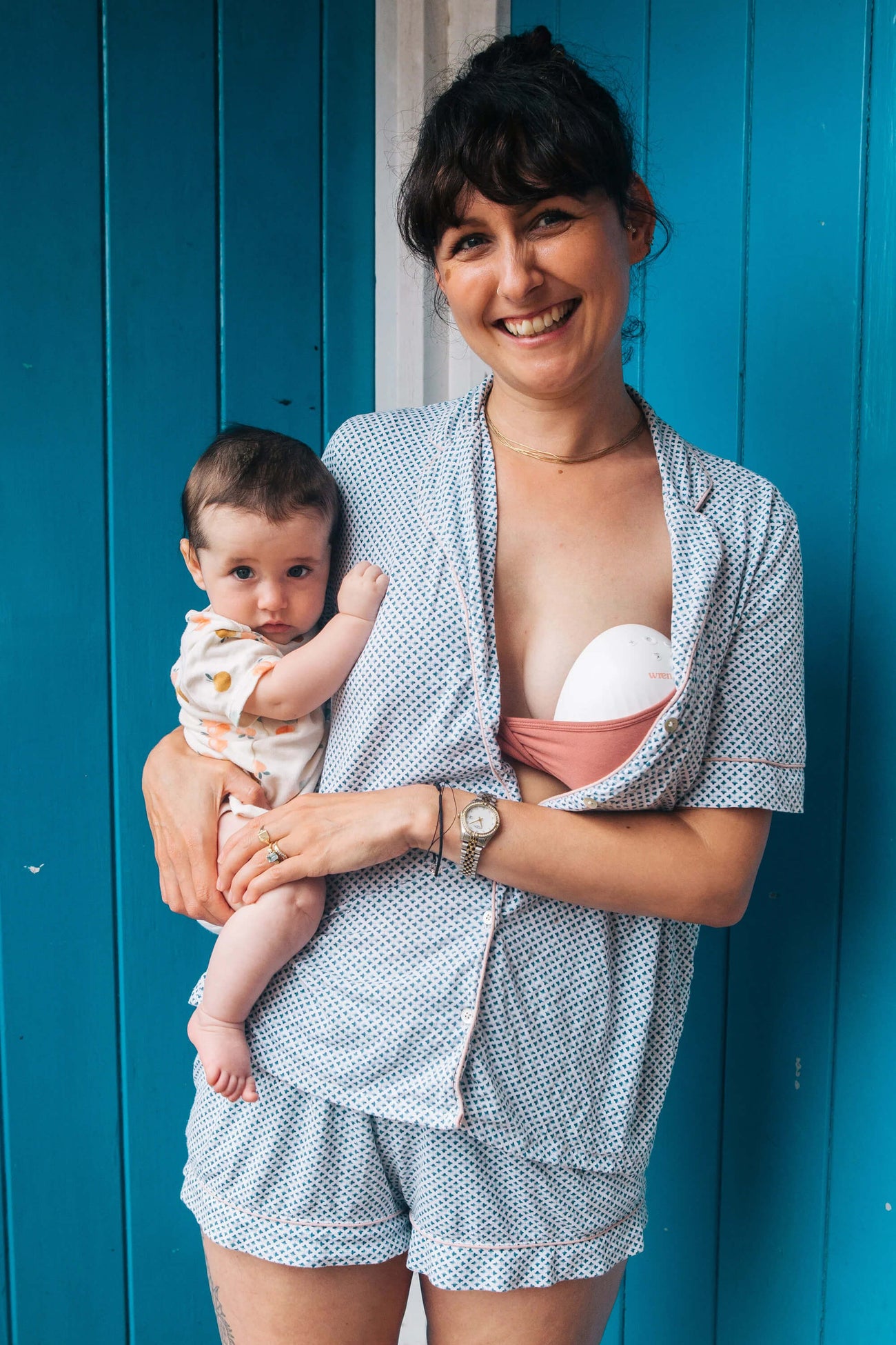 Woman wearing a Wren Hands Free Breast Pump, standing up holding her baby