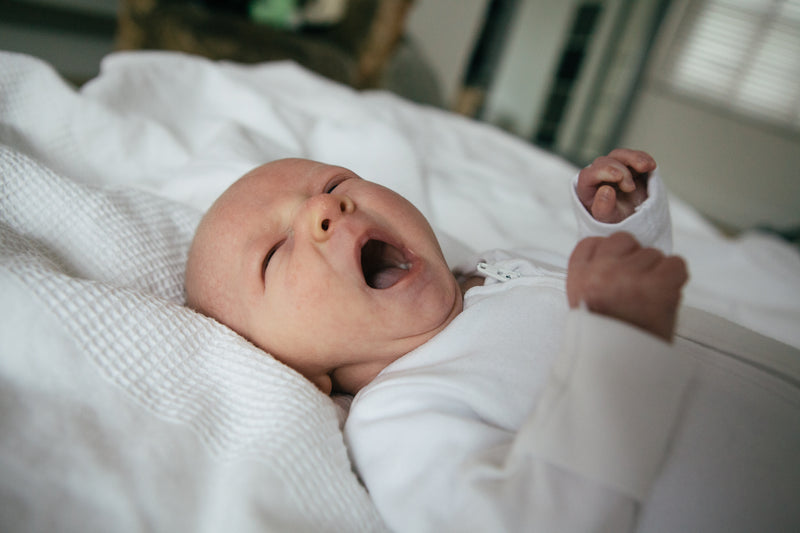 A baby yawning and stretching in bed