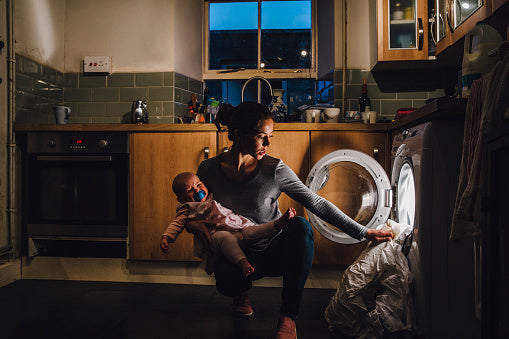 A woman holding her baby and pulling the washing out of the machine